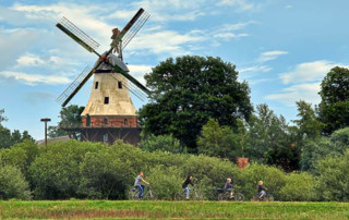 Eine Familien-Fahrradtour am Deich. Im Hintergrund ist die Mühle zu sehen.