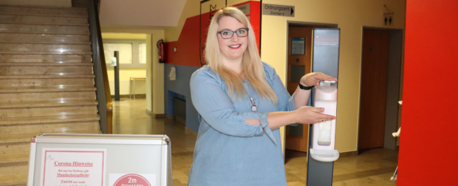 Yasmin Pyrchalla (Mitarbeiterin aus dem Standes- und Meldeamt) im Eingangsbereich des Rathauses, der mit einem Desinfektionsmittel-Spender und Informationsschildern mit Corona-Hinweisen ausgestattet wurde. Aufnahme: Wlodarczyk/Gemeinde Barßel