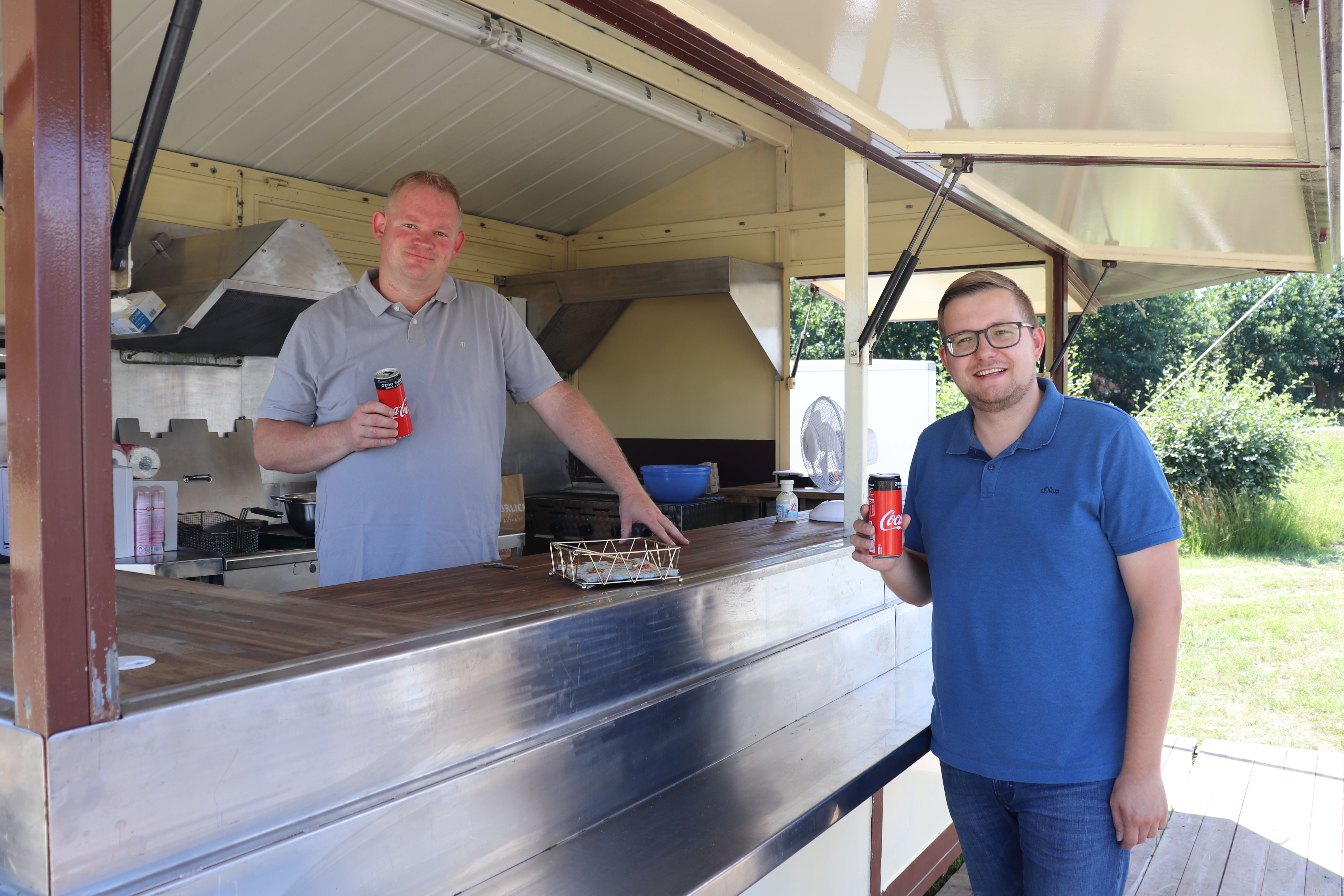 Oswald Eilers (links) und Bürgermeister Nils Anhuth trinken beim Aufbau des mobilen „Hafen-Cafés“ das erste Kaltgetränk. Aufnahme: Gemeinde Barßel