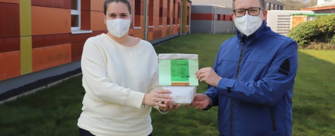 Barßels Bürgermeister Nils Anhuth brachte eine Tüte der Mischung „Bienenweide Nord-West“ in die Harkebrügger Grundschule, um sie Schulleiterin Nicole Lütjelüschen zu überreichen. Bildquelle: Johannes Passmann